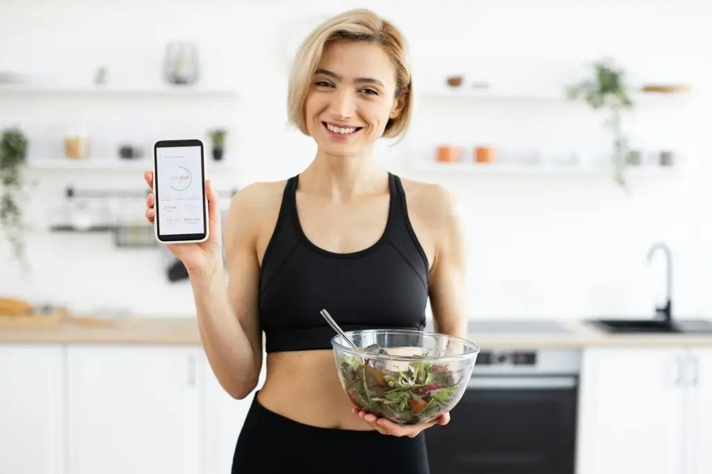 Woman in sportswear holding salad and displaying fitness app
