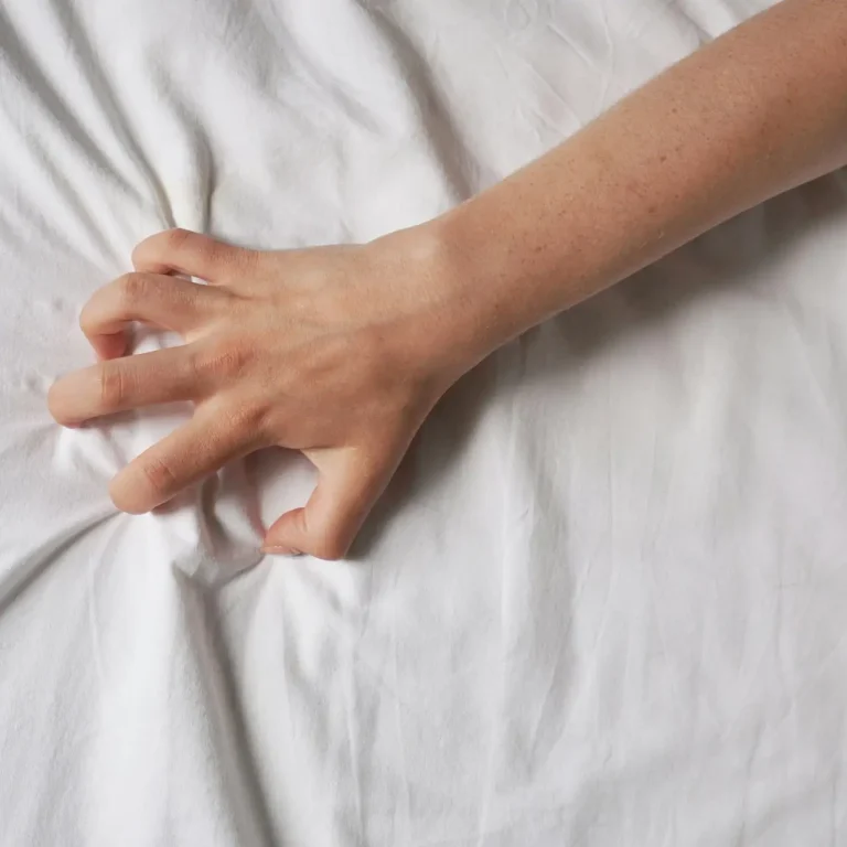hand of unrecognizable woman grabs bed sheet during sex